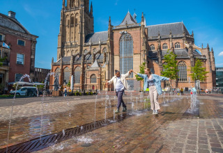 Twee mensen genieten van een fontein op een zonnig plein met een historische kerk op de achtergrond in Nederland.