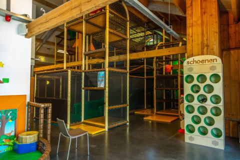 Indoor speeltuin in een vakantiepark met glamping, houten structuur en schoenenrek aan de zijkant.