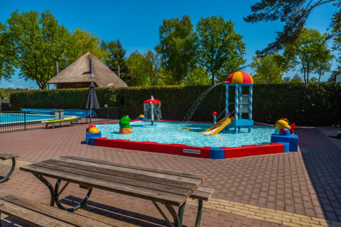 Kleurrijk kinderzwembad met glijbaan en speelelementen in een vakantiepark met glamping faciliteiten.