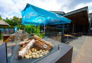 Buitenrestaurant met blauwe Heineken parasols, moderne vuurtafel, stoelen en tafels bij glamping park.