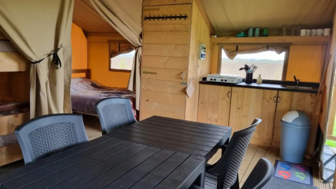 Vista interna di una tenda safari con tavolo da pranzo, cucina, letto a castello e matrimoniale a Boerderijcamping de Hinde.