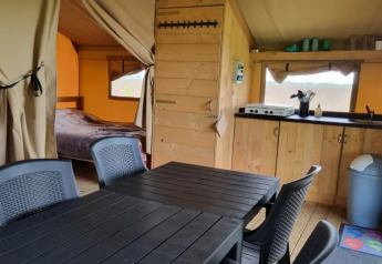 Indvendig visning af et safari telt med spisebord, køkken, køjeseng og dobbeltseng på Boerderijcamping de Hinde.