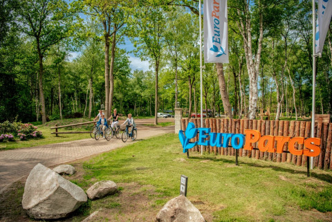 Ingang van EuroParcs vakantiepark met fietsende mensen en bord, omgeven door bomen en natuur.