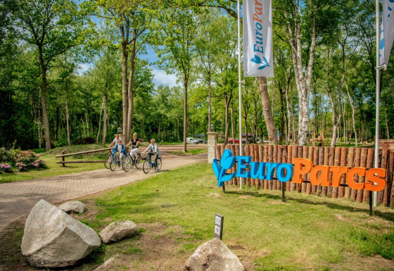 Ingang van EuroParcs vakantiepark met fietsende mensen en bord, omgeven door bomen en natuur.