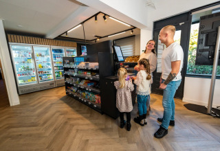 Gezin rekent af bij een zelfbedieningskassa in een kleine supermarkt van een vakantiepark met glamping.