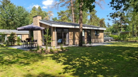 Lodge moderne avec un grand jardin, espace repas extérieur et entouré de grands arbres verdoyants.