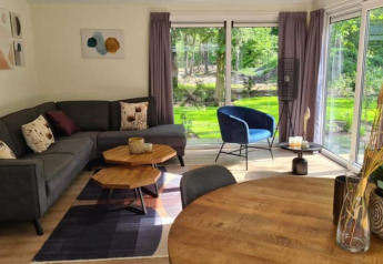 Modern lodge living room with gray sectional sofa, blue chair, large windows, wood table, and garden view.
