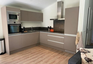 Cocina moderna de alojamiento con suelo de madera, armarios grises y electrodomésticos integrados.