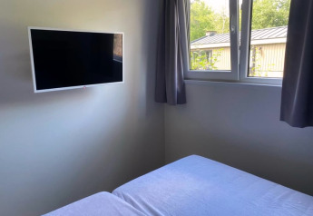 Hoekkamer in een lodge met wand-gemonteerde tv, raam met gordijnen en zicht op het groen buiten.