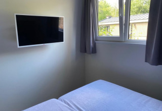 Habitación de esquina en una cabaña con televisor de pantalla plana en la pared y ventana con cortinas y vista exterior.