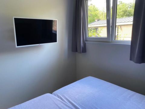 Habitación de esquina en una cabaña con televisor de pantalla plana en la pared y ventana con cortinas y vista exterior.