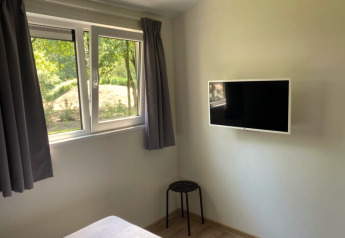 Lichte lodgekamer met een groot raam, wand-gemonteerde tv, grijze gordijnen en zwarte kruk.