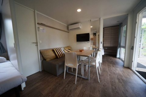 Hébergement glamping moderne avec canapé, table à manger, TV à écran plat et sol aspect bois.