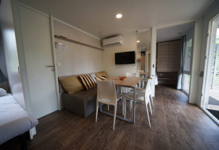 Hébergement glamping moderne avec canapé, table à manger, TV à écran plat et sol aspect bois.