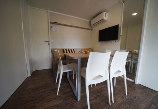 Hébergement de glamping moderne avec table à manger, chaises blanches, canapé, télévision et climatisation.