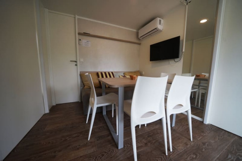 Hébergement de glamping moderne avec table à manger, chaises blanches, canapé, télévision et climatisation.