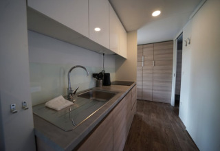 Glamping-keuken met moderne spoelbak, houten kasten en houten vloer, zicht op bergruimte.