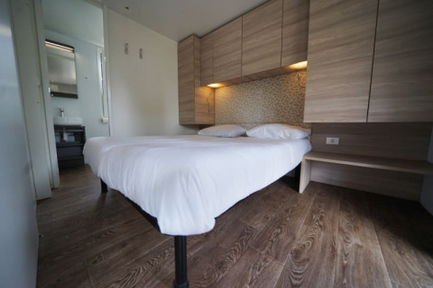 Hébergement glamping moderne avec lit double, sol en bois, rangements clairs et accès à la salle de bain.