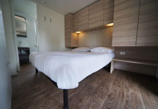 Hébergement glamping moderne avec lit double, sol en bois, rangements clairs et accès à la salle de bain.