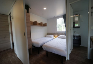 Alojamiento glamping moderno con dos camas individuales, suelo de madera, estantería y baño privado.