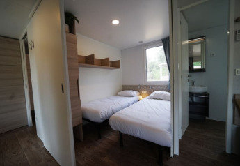 Alojamiento glamping moderno con dos camas individuales, suelo de madera, estantería y baño privado.