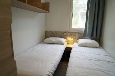 Hébergement de glamping moderne avec deux lits simples, draps blancs, fenêtre et décor minimaliste.