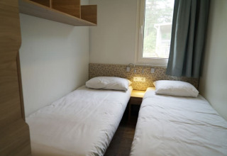 Hébergement de glamping moderne avec deux lits simples, draps blancs, fenêtre et décor minimaliste.