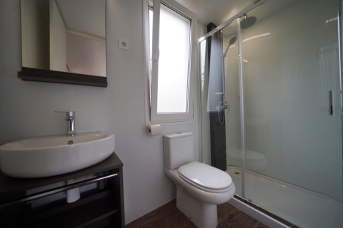 Salle de bain moderne dans un hébergement glamping avec douche, WC, lavabo et miroir mural.