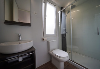 Moderne badkamer in glampingverblijf met douche, toilet, wastafel en een spiegel aan de muur.