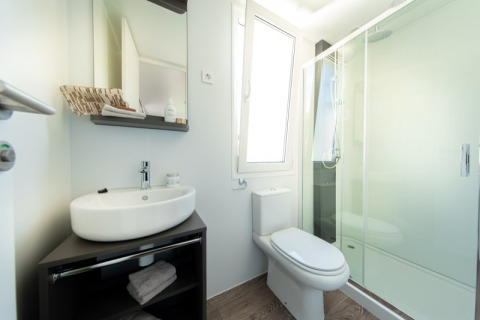 Modernes Badezimmer in einer Lodge mit Waschbecken, Spiegelschrank, WC, Fenster und Glasduschkabine.