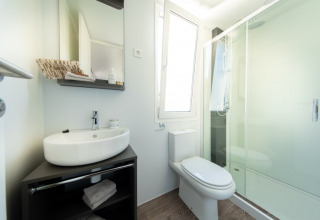 Modernes Badezimmer in einer Lodge mit Waschbecken, Spiegelschrank, WC, Fenster und Glasduschkabine.