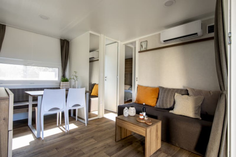 Interior de una moderna cabaña con suelo de madera, mesa de comedor, sofá con cojines y aire acondicionado.