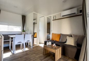 Intérieur de lodge moderne avec sol en bois, table à manger, canapé à coussins et climatisation murale.