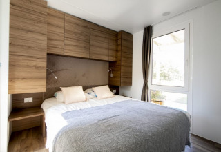 Dormitorio moderno de lodge con cama doble, armarios de madera, grandes ventanas y luz natural.