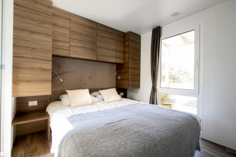 Chambre moderne de lodge avec lit double, armoires en bois, grandes fenêtres et lumière naturelle.