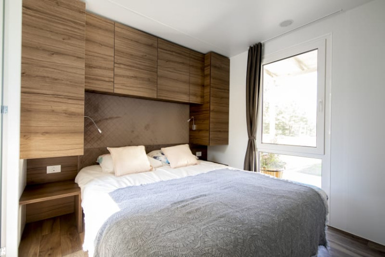 Dormitorio moderno de lodge con cama doble, armarios de madera, grandes ventanas y luz natural.