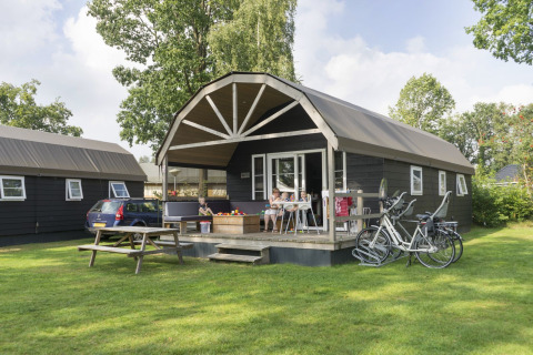 Familia relajándose en una Vechtdallodge en Kampeerdorp de Zandstuve, Países Bajos, con bicicletas y coche.