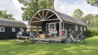 Familia relajándose en una Vechtdallodge en Kampeerdorp de Zandstuve, Países Bajos, con bicicletas y coche.