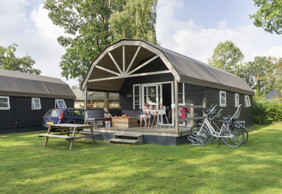 Familie slapper af foran en Vechtdallodge på Kampeerdorp de Zandstuve, Holland, med cykler og bil.