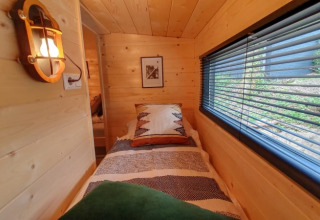 Et hyggeligt soveværelse med trævægge, enkeltseng, stort vindue med persienner i et tiny house.