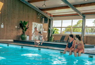 Gezellige sfeer in het binnenzwembad van een vakantiepark met glamping, waar gezinnen samen ontspannen.