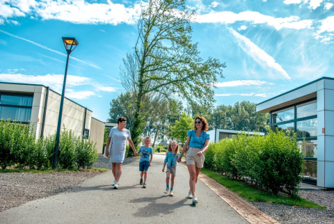 Gezin wandelt samen op zonnige dag door een vakantiepark met moderne glamping accommodaties en veel groen.