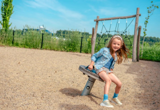Meisje speelt op een schommel in een speeltuin bij een vakantiepark met glampingaccommodaties in de natuur.