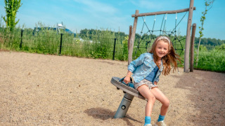 Meisje speelt op een schommel in een speeltuin bij een vakantiepark met glampingaccommodaties in de natuur.
