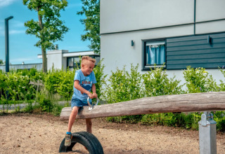 Een jonge jongen speelt op een wip bij een vakantiepark met glamping-accommodaties en moderne huizen.