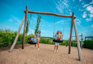 Kinderen spelen op schommels terwijl een volwassene duwt op een zonnige dag in een vakantiepark met glamping.
