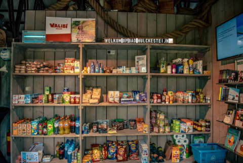 Winkelrekken in een vakantiepark met diverse snacks, drankjes en huishoudproducten, ideaal voor kampeerders.