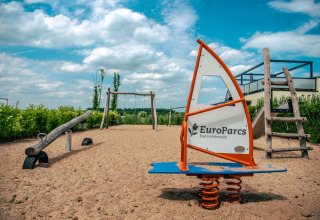 Speeltuin met schommel, wip en veerwip bij EuroParcs Bad Hulckesteijn glamping onder een blauwe lucht.