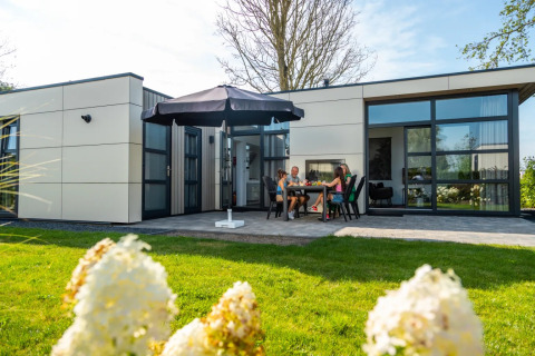 Gezin geniet van een maaltijd onder een parasol op het terras van een moderne glamping accommodatie.