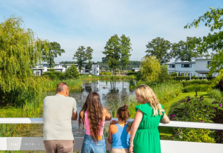 Gezin geniet van het uitzicht op een vijver in een vakantiepark met luxe glamping accommodaties in het groen.